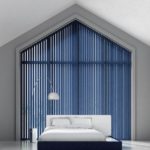 indigo blue vertical window blinds covering a very large pentagon shaped window behind a bed