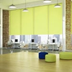bright lime yellow coloured roller window blinds covering huge windows in a large modern open plan converted warehouse style corporate office