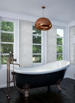 marble coloured vertical window blinds covering multiple windows in a modern bathroom with a large roll top bath