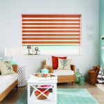 roller window blind with alternating horizontal stripes of bright orange and translucent white covering a window in a colourful living room
